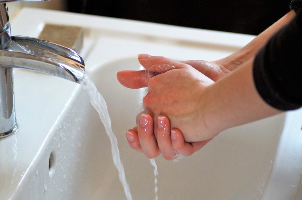 Person their hands in a white sink with water flowing